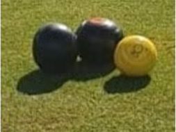 Two black bowls and a yellow jack on the crown green